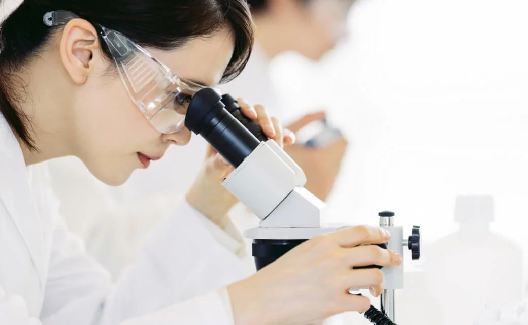 Nhà nghiên cứu đeo kính bảo hộ quan sát mẫu dưới kính hiển vi trong phòng thí nghiệm