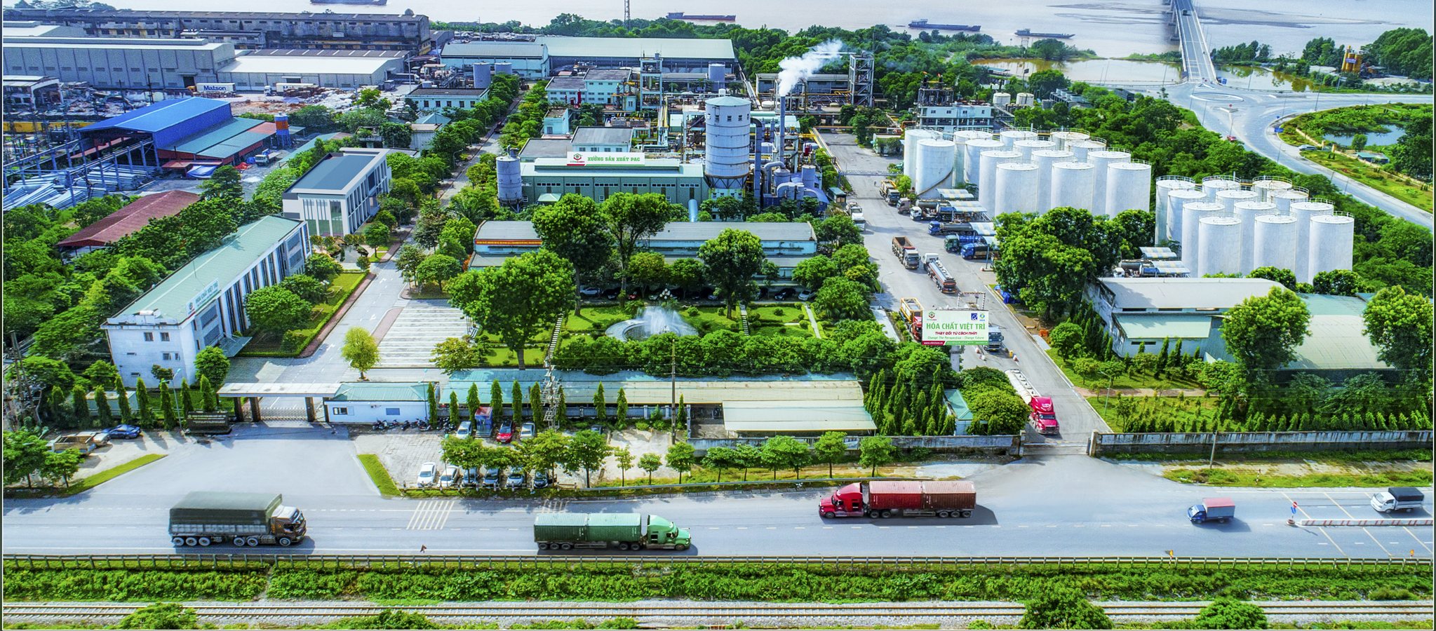 Toàn cảnh nhà máy Hóa chất Việt Trì nhìn từ trên cao bên bờ sông, cụm bồn chứa trắng, nhà xưởng mái xanh và cây xanh